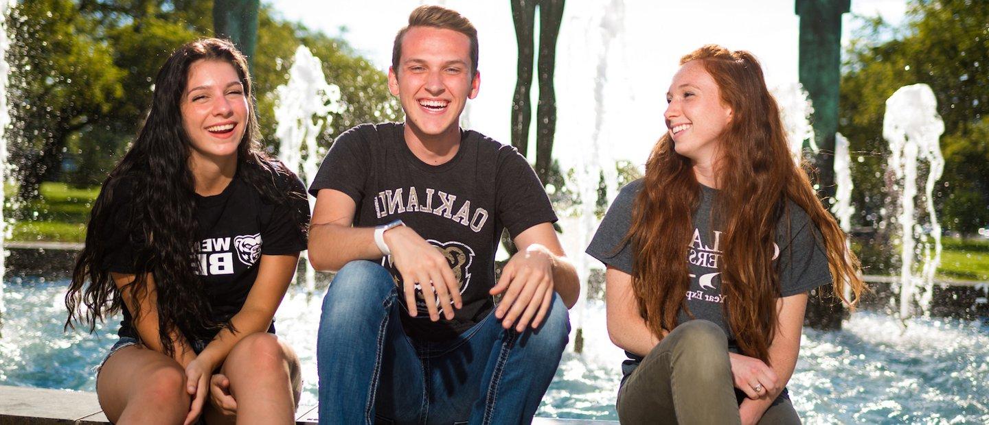 三个十大菠菜台子的学生坐在喷泉边，笑个不停.