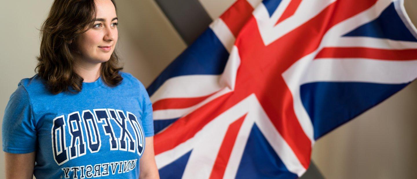 A girl wearing an Oxford University shirt, posing in front of a British flag.