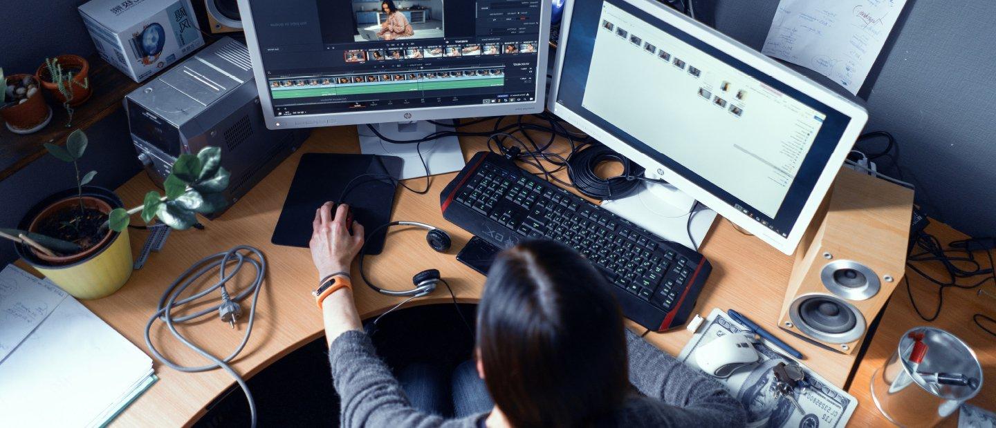 A student editing film at a computer desk.