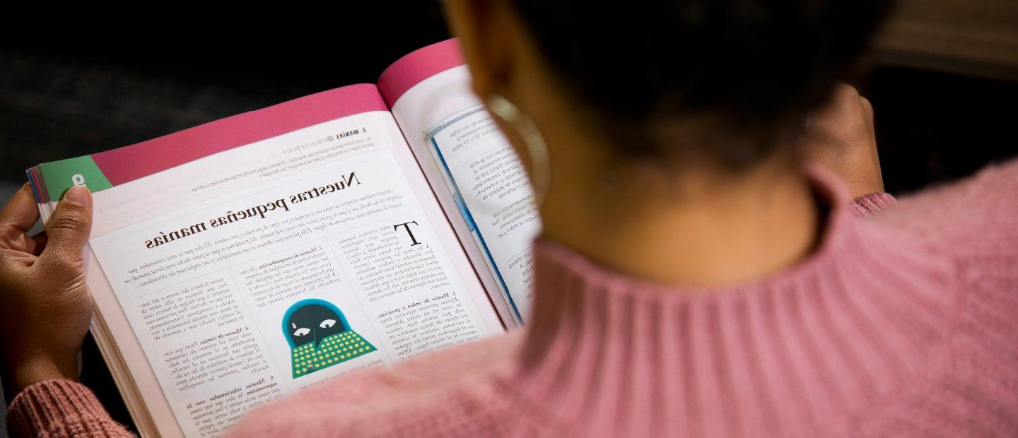 A woman reading a Spanish language textbook.