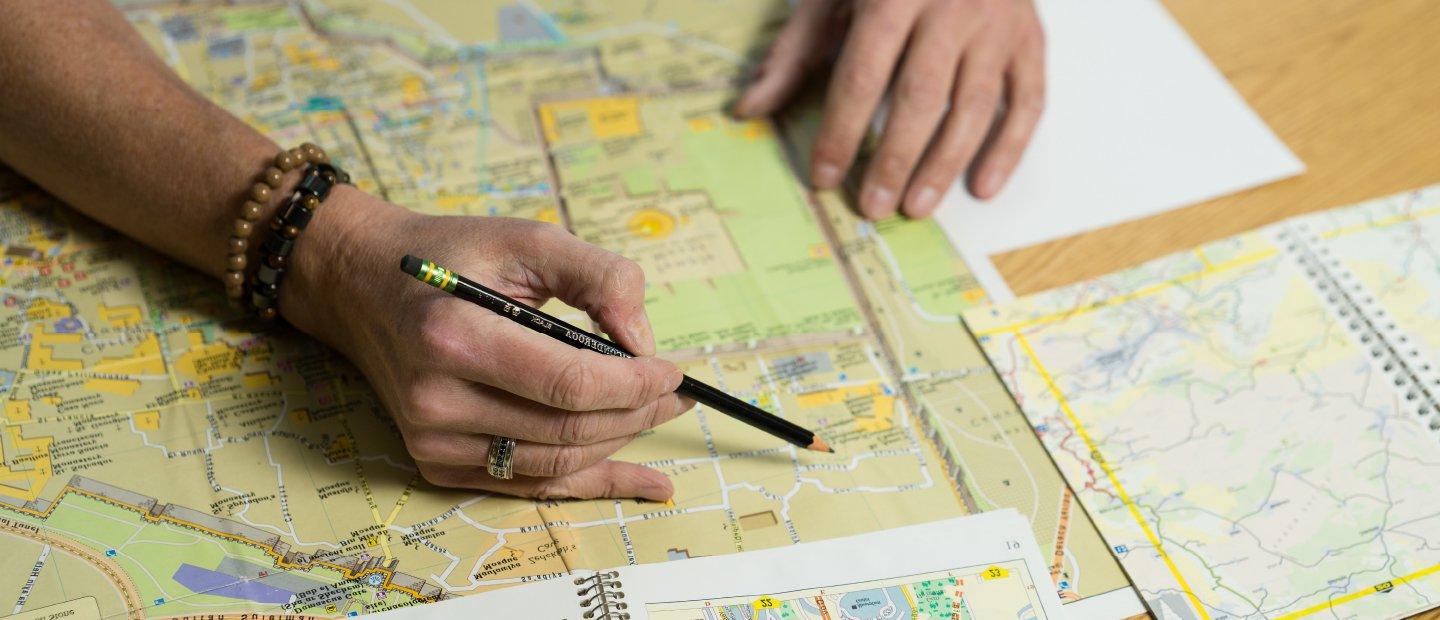 A person holding a pencil over a location on a map.