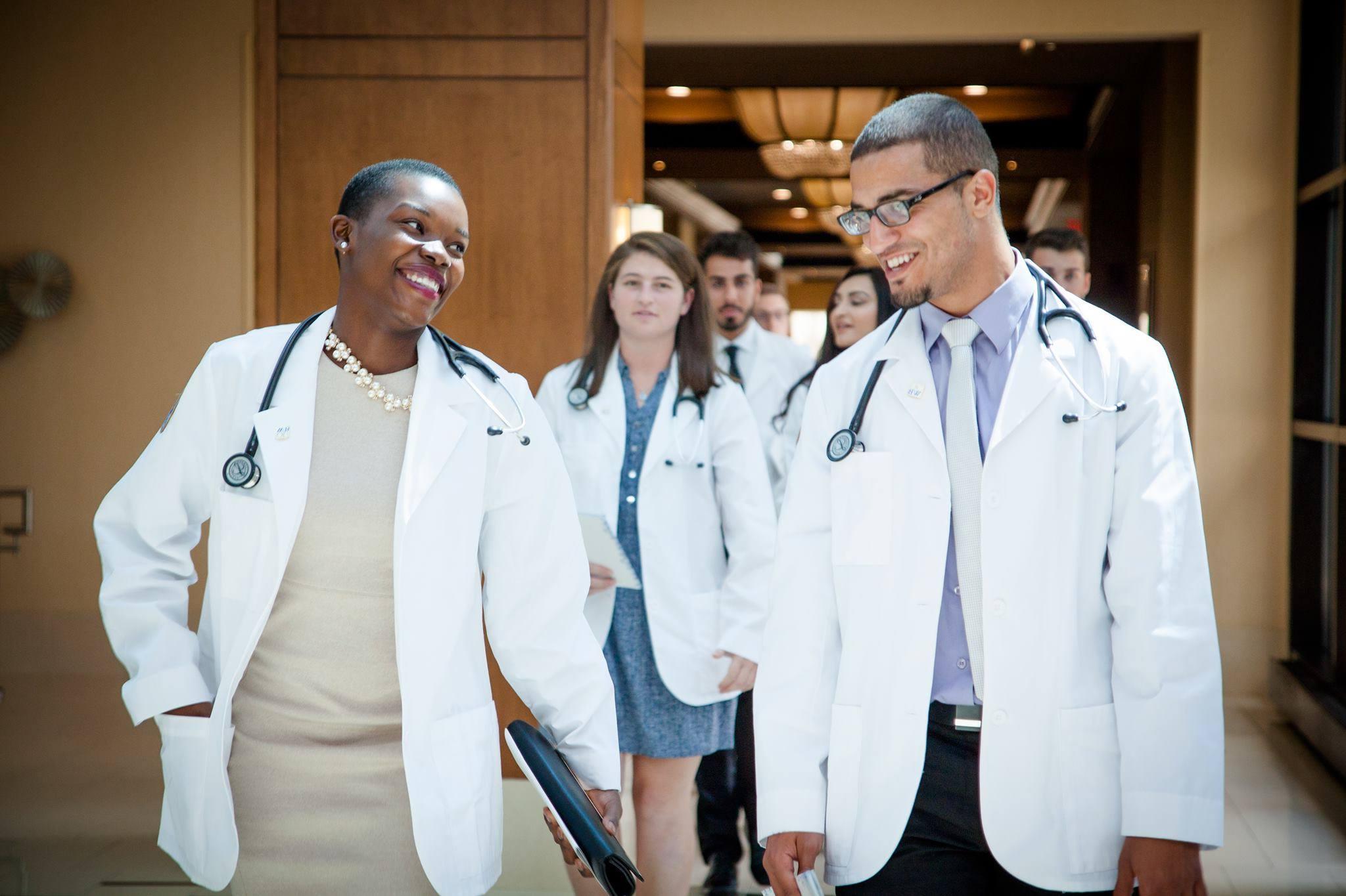 Two students walk out of the White Coat ceremony wearing their coats.