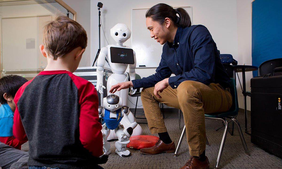 坐在椅子上的男子向两个孩子展示机器人