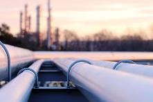 A close up image of oil pipelines with an industrial building in the background.