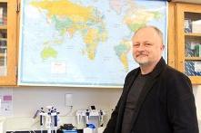 Biology Professor Taras Oleksyk standing in front of a map on the wall.